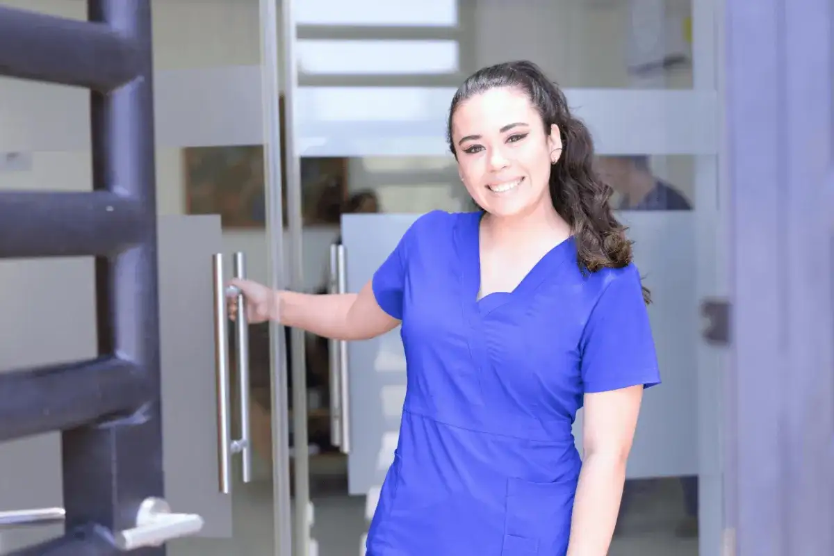 Uśmiechnięta pielęgniarka w niebieskim uniformie otwiera drzwi. Czy zastanawiasz się, ile zarabia pielęgniarka pediatryczna?