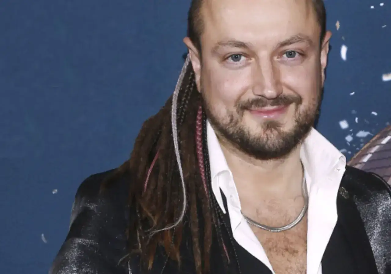 Aleksander Milwiw-Baron, znany z charakterystycznych dredów, z uśmiechem na twarzy. Jego pochodzenie jest często tematem dyskusji.