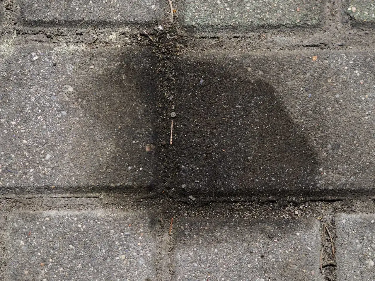 Stare plamy z oleju na kostce brukowej tworzą ciemny, rozlany kształt, świadcząc o dawnych wyciekach.