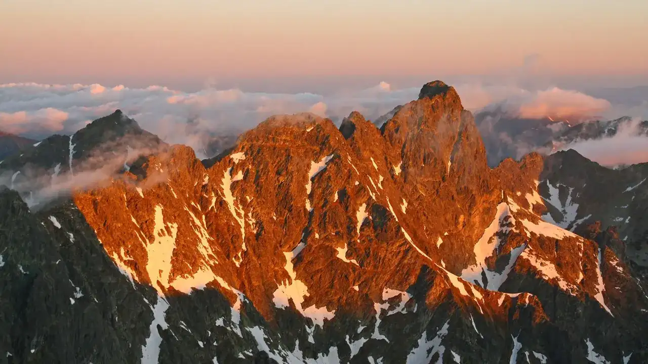 Zachód słońca maluje na pomarańczowo skaliste zbocza, a śnieg lśni na tle chmur. Widok na mięguszowiecki szczyt czarny zapiera dech.