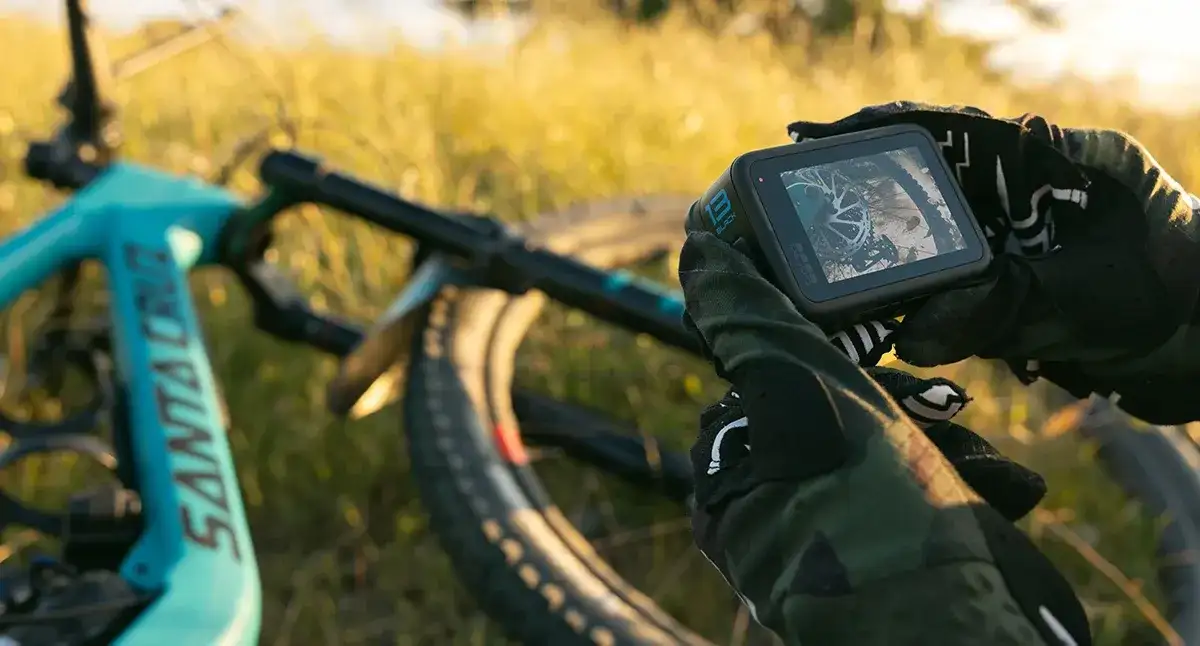 Ręce w rękawicach trzymają kamerę GoPro, gotową do nagrywania zjazdów na rowerze górskim. Niesamowite gopro zdjęcia czekają!