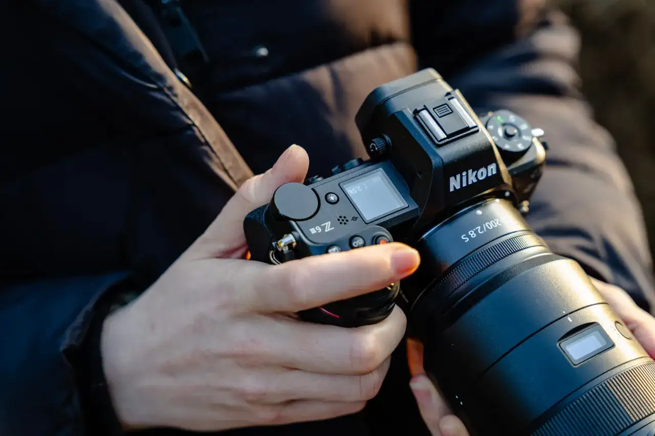 Dłonie trzymają aparat Nikon Z6 III z obiektywem.