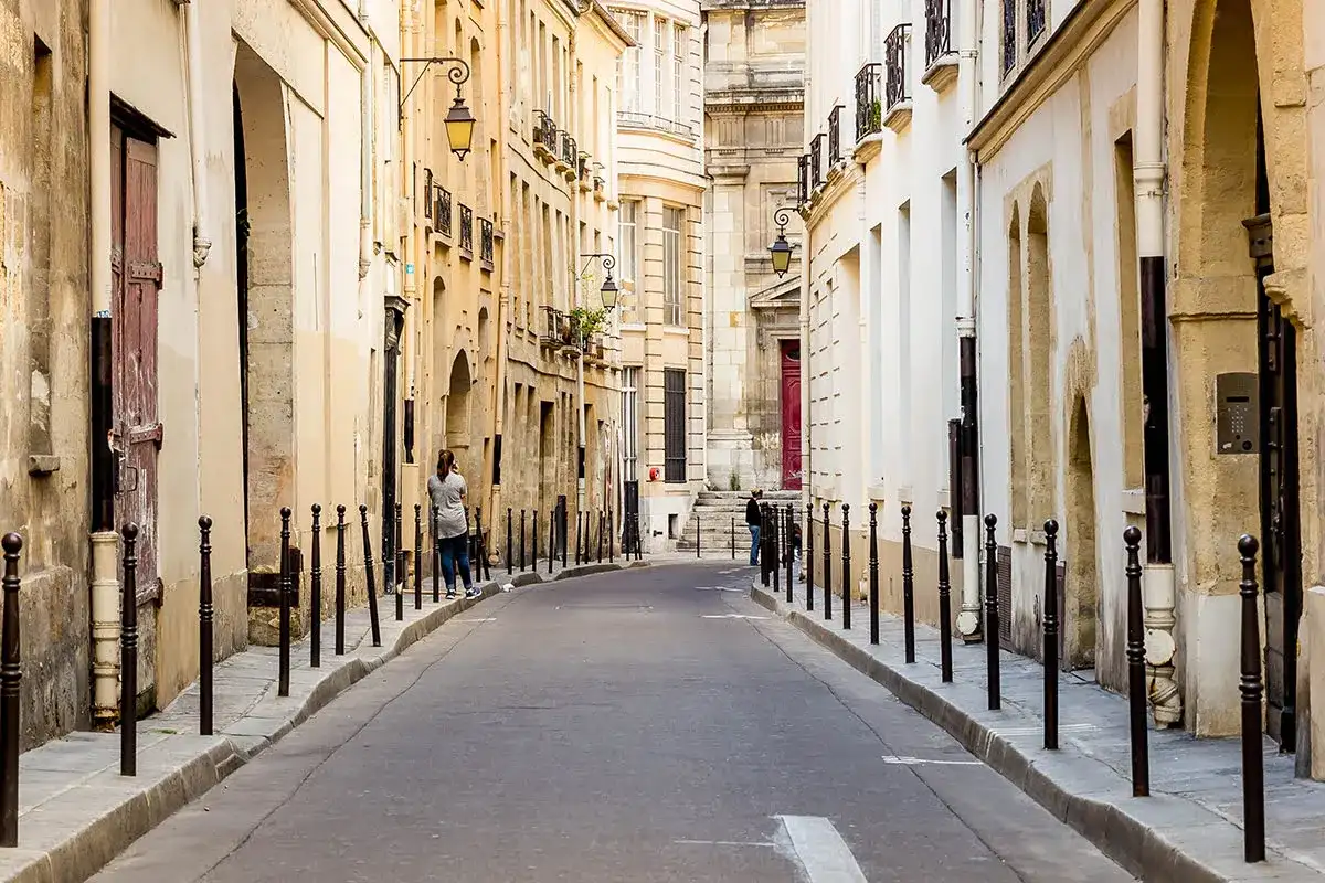 Urokliwa uliczka w paryskiej dzielnicy Le Marais, z kamiennymi budynkami i latarniami.