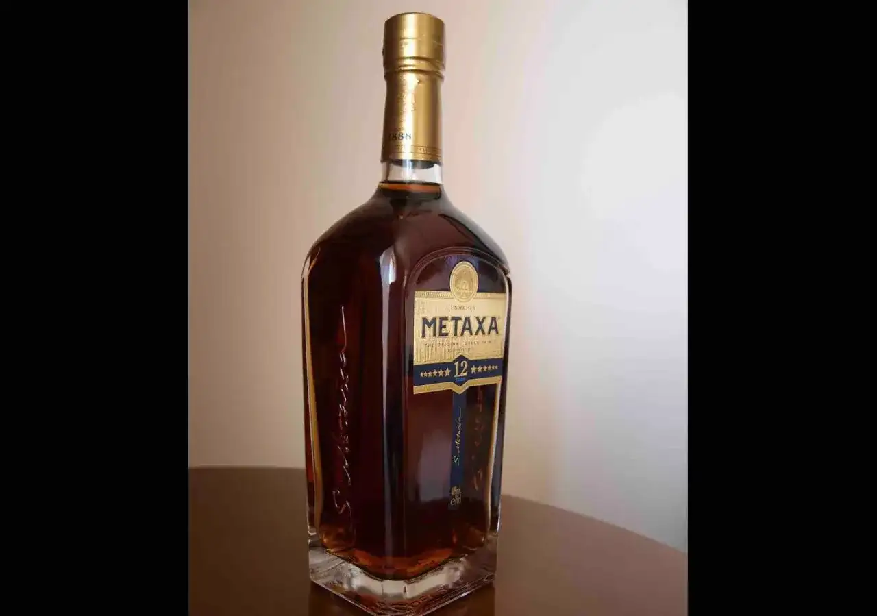 Butelka greckiego brandy Metaxa 12 gwiazdek na stole.