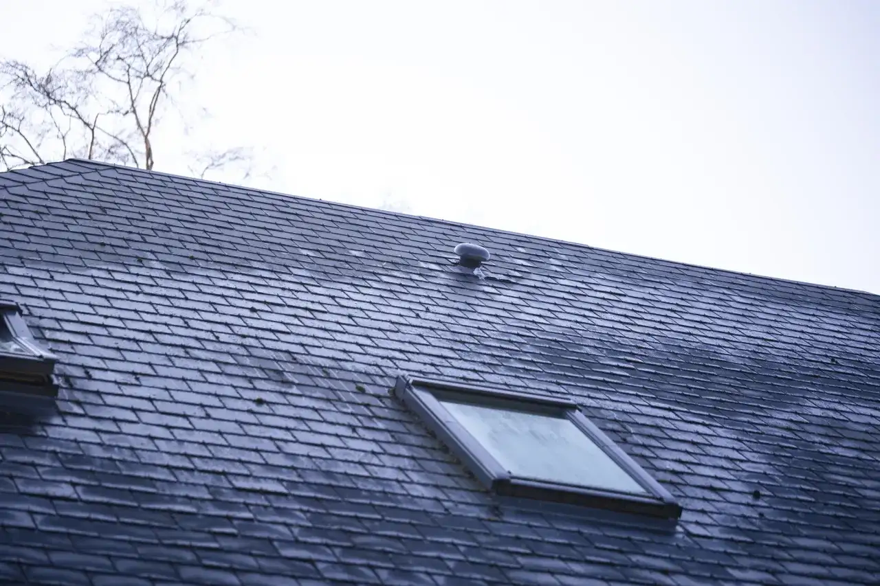 Dach pokryty ciemną dachówką betonową płaską, z widocznym oknem dachowym i kominkiem wentylacyjnym.