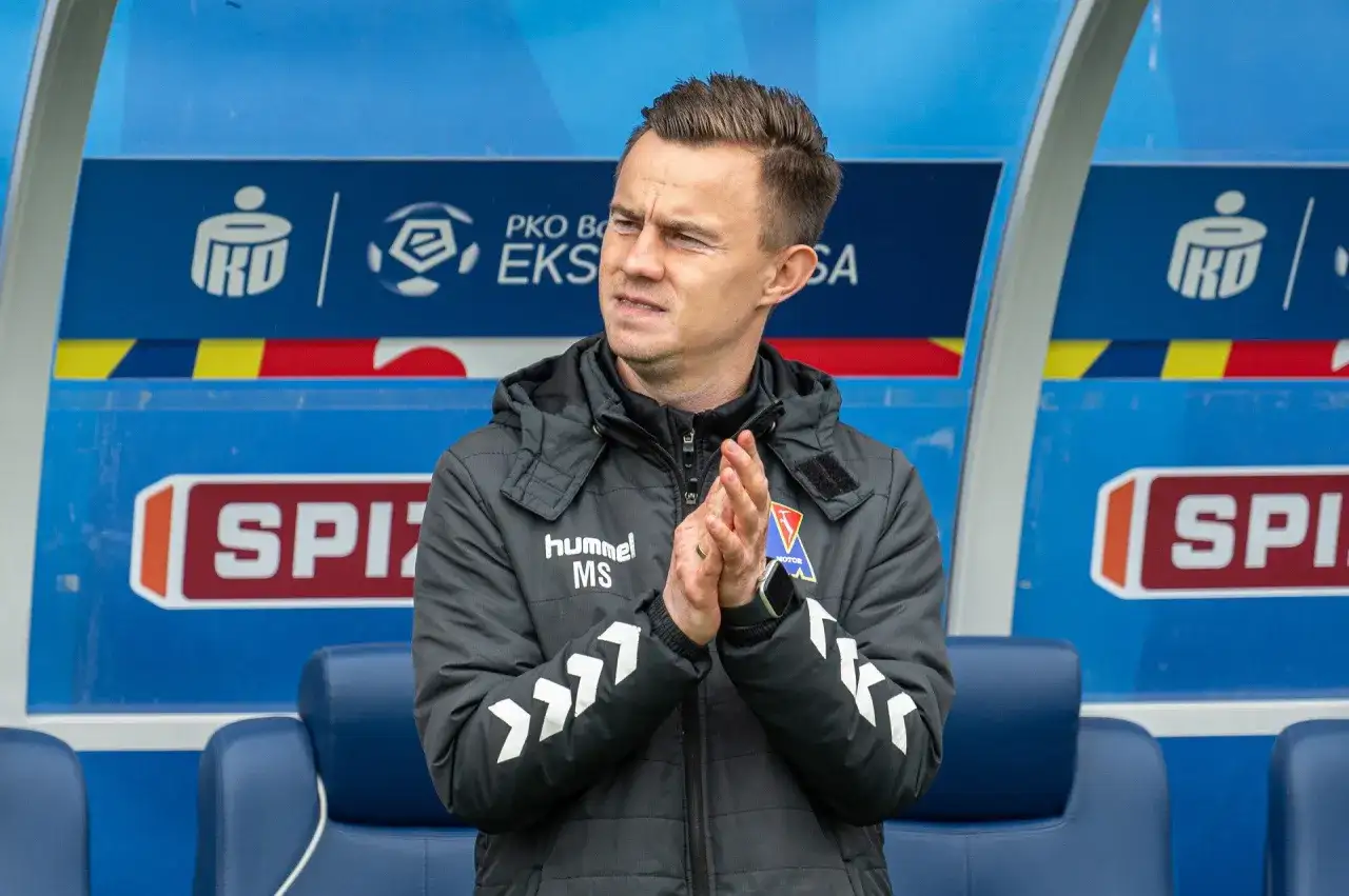 Trener z PKO BP Ekstraklasa w TVP, kiedy? Mężczyzna w kurtce z logo "hummel" klaszcze na ławce rezerwowych.