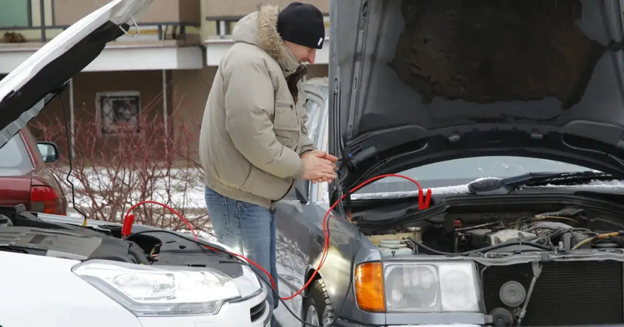 Mężczyzna próbuje odpalić auto zepsutym rozrusznikiem, używając kabli rozruchowych.