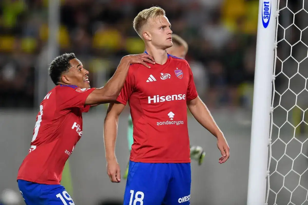 Piłkarze w czerwonych koszulkach świętują bramkę. Jeden z nich, z numerem 18, jest w centrum uwagi, a drugi gratuluje mu, być może to przyszli najlepsi strzelcy ekstraklasy.