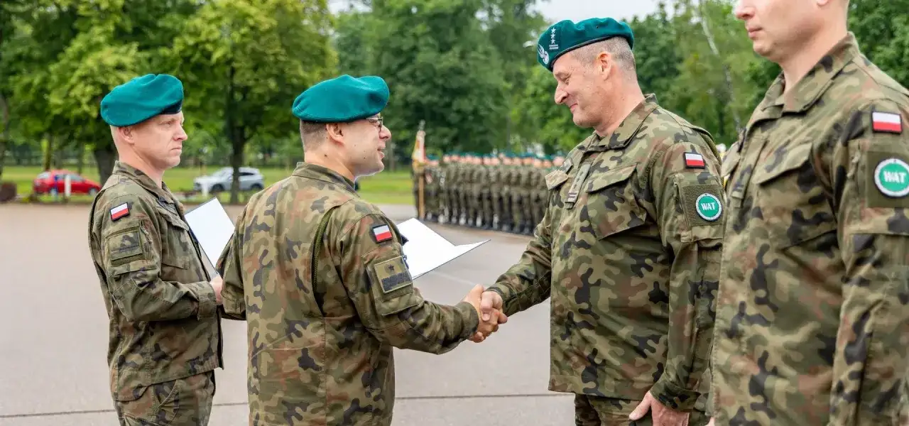 Żołnierze w mundurach i zielonych beretach podają sobie ręce, jeden z nich trzyma dokument.