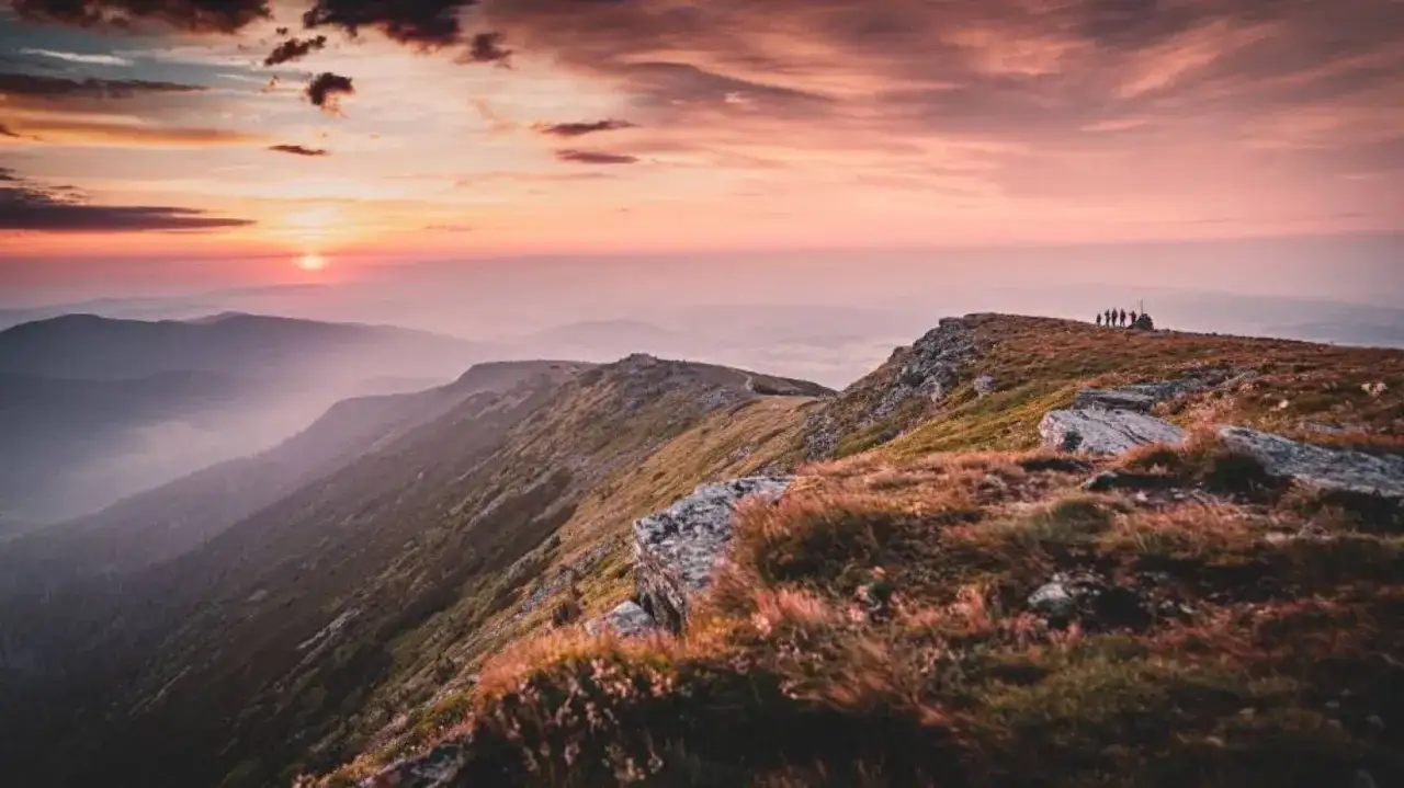 Zachód słońca nad pasmem górskim. Grupa turystów na szczycie, podziwiająca widok. Piękne, jakie góry!