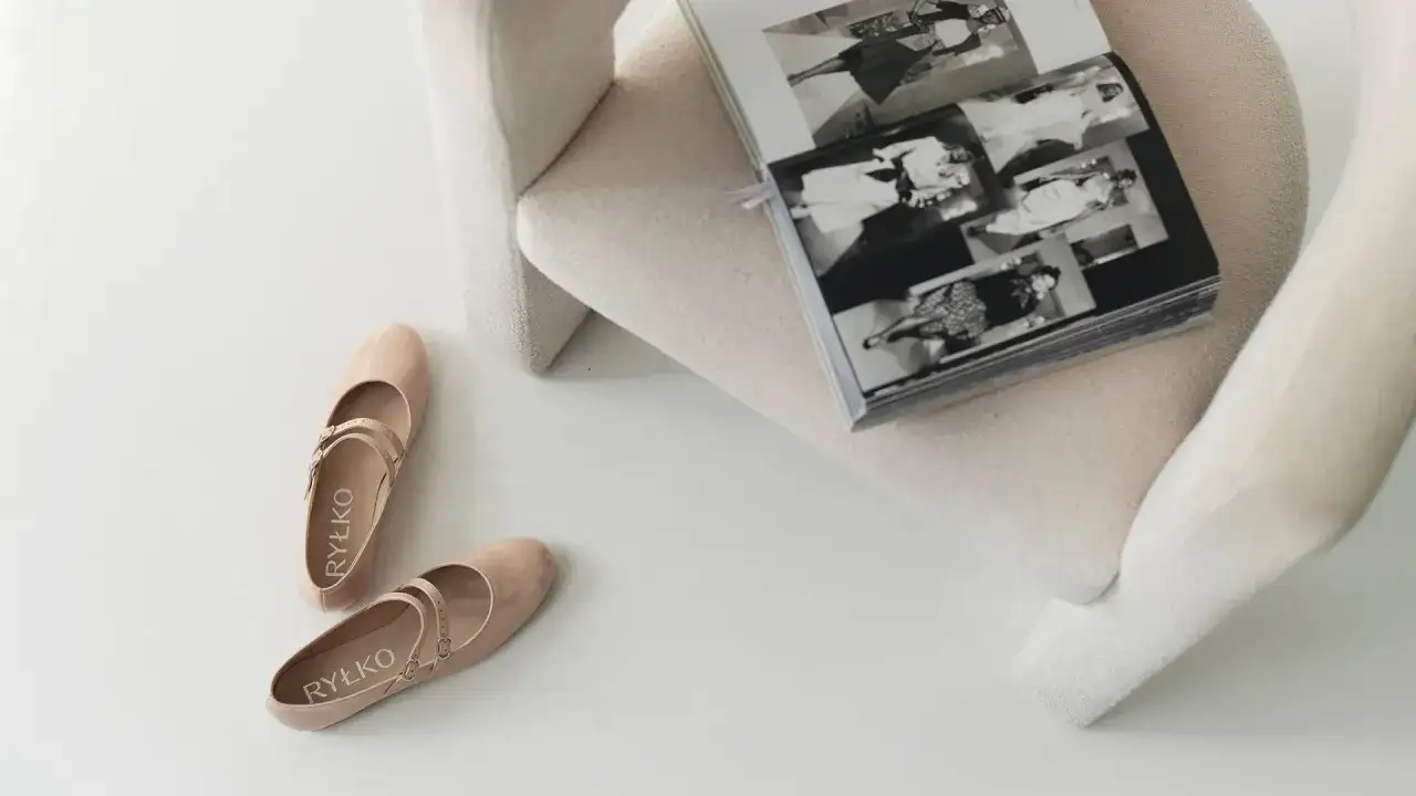 Beżowe baleriny Ryłko z paskiem, idealne, by dowiedzieć się, jak zmiękczyć buty na pięcie. Obok otwarta księga.