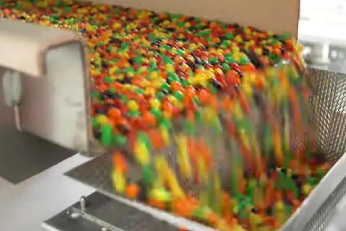 Kolorowe drażetki spadają z taśmociągu. Czy skittles są bezglutenowe? To pytanie nurtuje wielu łasuchów.