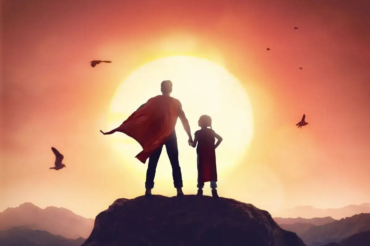 Ojciec i córka w pelerynach superbohaterów stoją na szczycie góry, patrząc na zachód słońca. To jak cytaty ojca do syna, pełne siły i miłości.