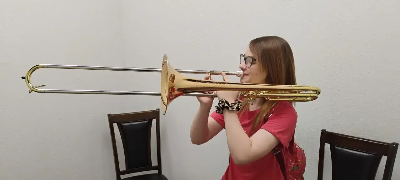 Dziewczyna gra na instrumencie dętym z suwakiem, ćwicząc trudne dźwięki.