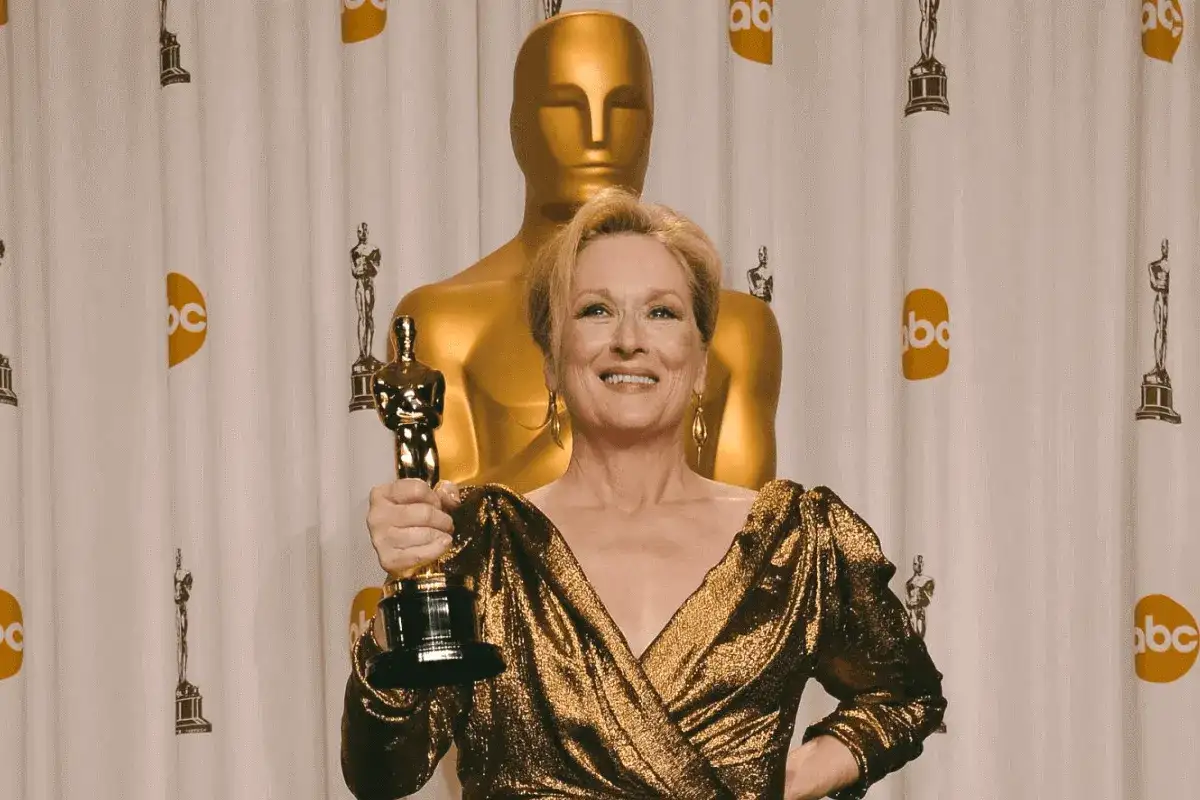 Meryl Streep z Oscarem, aktorka, która zdobyła najwięcej oscarów w XXI wieku, pozuje na tle złotych statuetek.