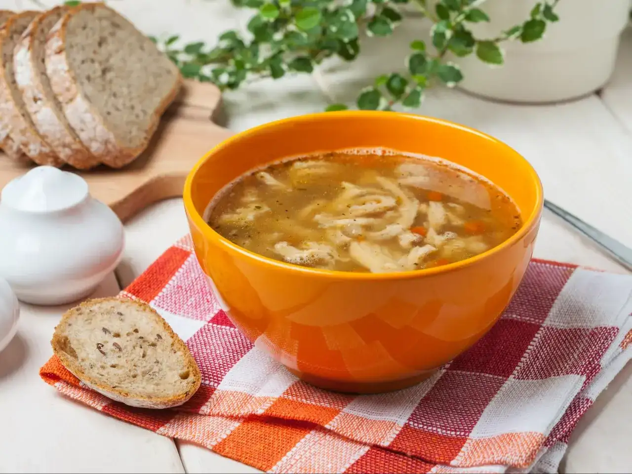 Gorąca zupa flaki w pomarańczowej misce, obok kromki chleba. Idealne do flaków są świeże dodatki.