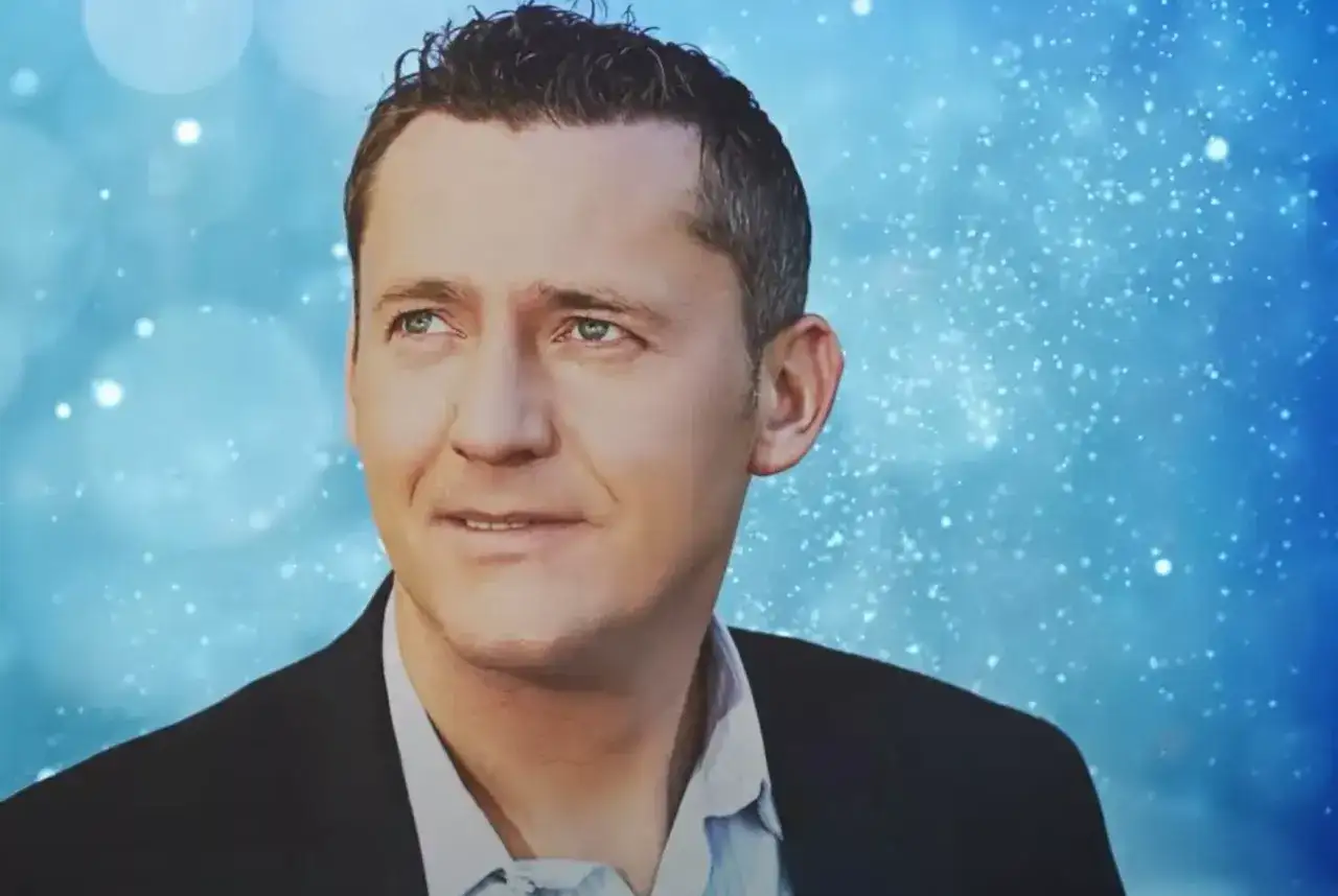 Portret Adama Chroli w garniturze na tle niebieskich, migoczących świateł.