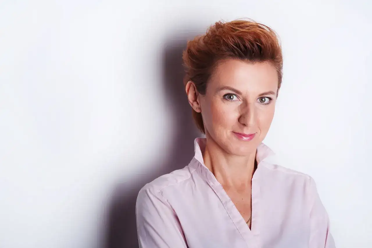 Kobieta z rudymi włosami w jasnoróżowej koszuli, uśmiecha się do obiektywu. Idealne miejsce do robienia zdjęć.