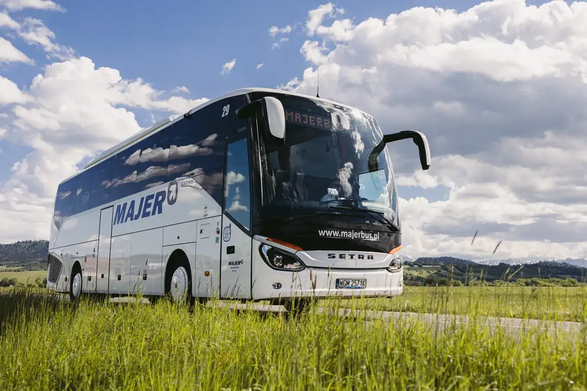 Autobus Majer na trasie Kraków - Mszana Dolna jedzie przez zielone pola pod błękitnym niebem.