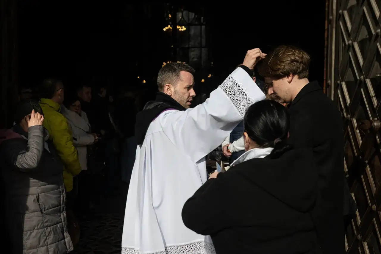 Ksiądz posypuje popiołem głowę wiernego przed kościołem.