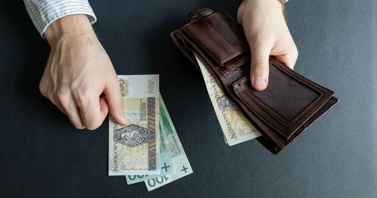Ręce trzymają polskie banknoty i brązowy portfel. Czy to początek wzrostu renty alkoholowej o 5% od marca 2026?