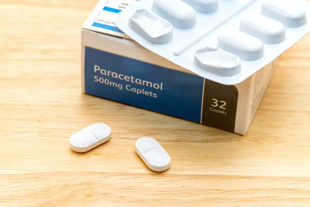 Opakowanie Paracetamolu 500mg, leki na ból kręgosłupa szyjnego, leżą na drewnianym blacie obok dwóch tabletek.