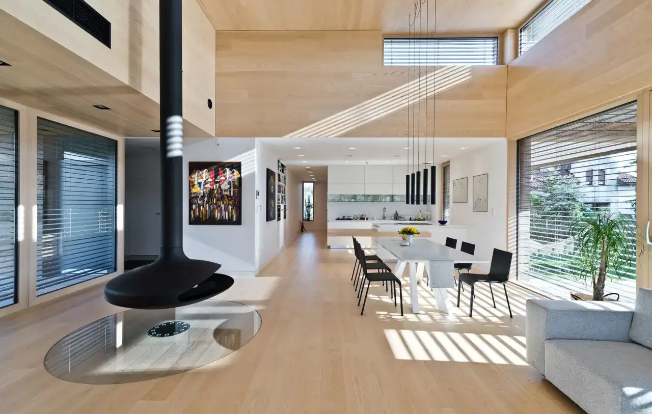 Nowoczesne wnętrze z kominkiem i jadalnią, gdzie doświetlenie pomieszczeń światłem naturalnym tworzy grę cieni na drewnianej podłodze.