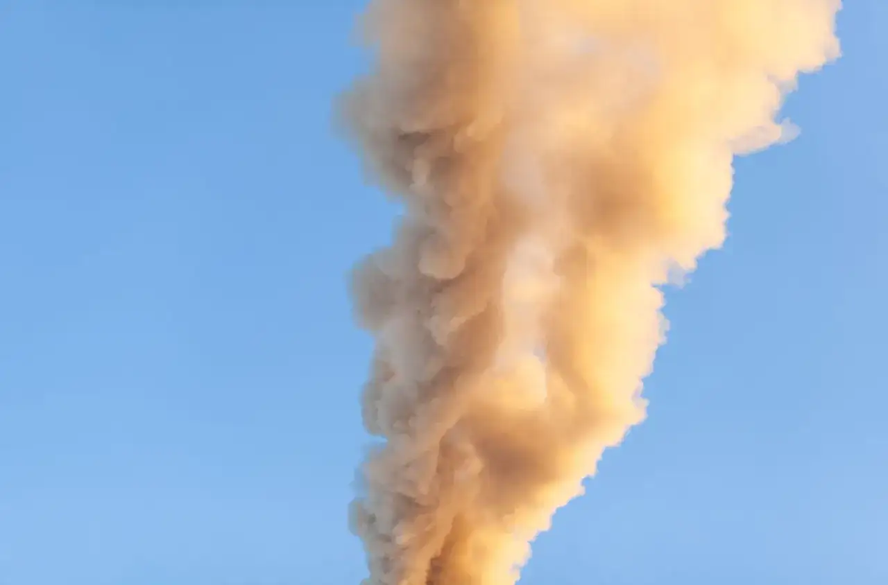 Gęsty, żółty dym z komina unosi się na tle błękitnego nieba. To znak, że coś się dzieje w fabryce.