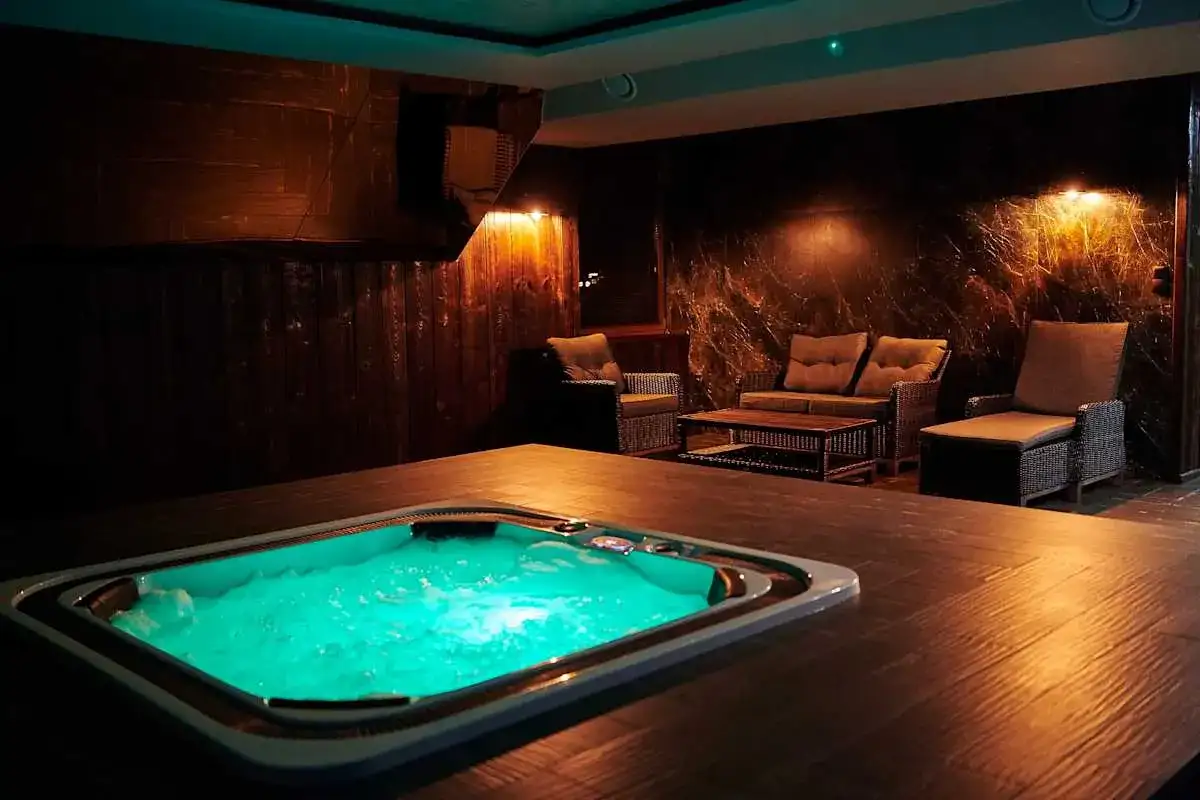 Wanna z zielonym podświetleniem i meble wypoczynkowe w przytulnym wnętrzu spa.