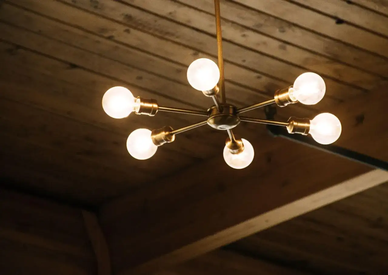 Nowoczesny żyrandol na dwa włączniki, z sześcioma żarówkami, zamontowany na drewnianym suficie.