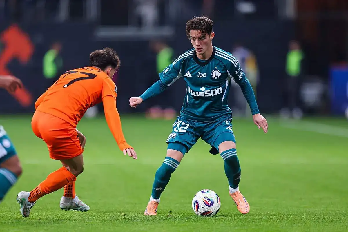 Piłkarz Legii Warszawa z piłką przy nodze, w walce z zawodnikiem Pogoni Szczecin.