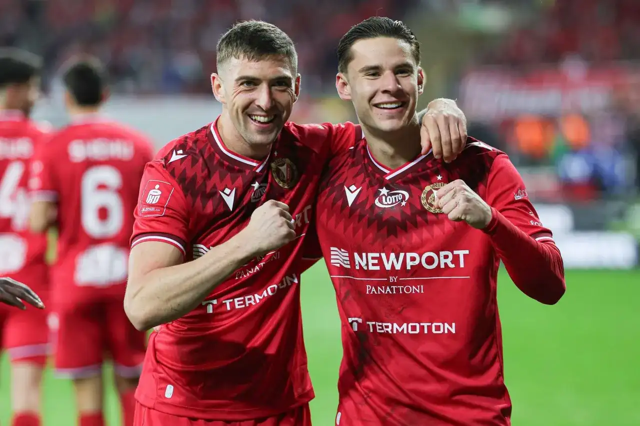 Dwóch piłkarzy w czerwonych koszulkach świętuje na boisku.