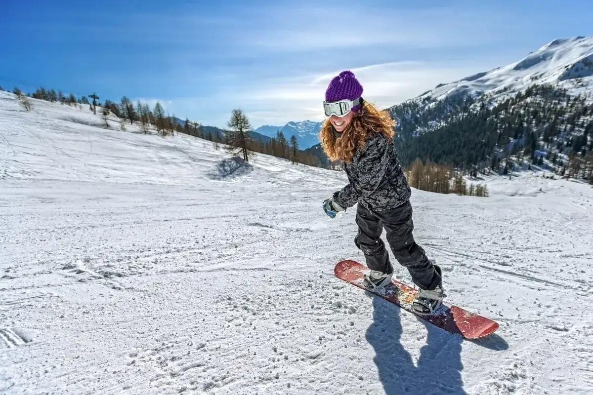 Dziewczyna na snowboardzie, z uśmiechem na twarzy, zjazdem po stoku. Warto wiedzieć, jak ustawić wiązania snowboard, by jazda była bezpieczna i przyjemna.