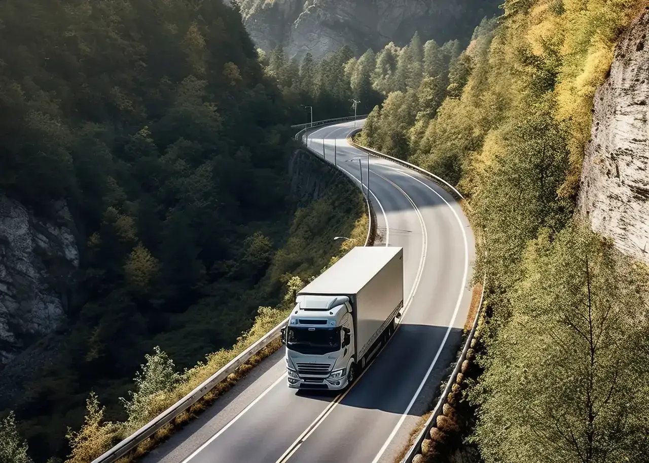 Ciężarówka z naczepą na krętej drodze w górskim krajobrazie.