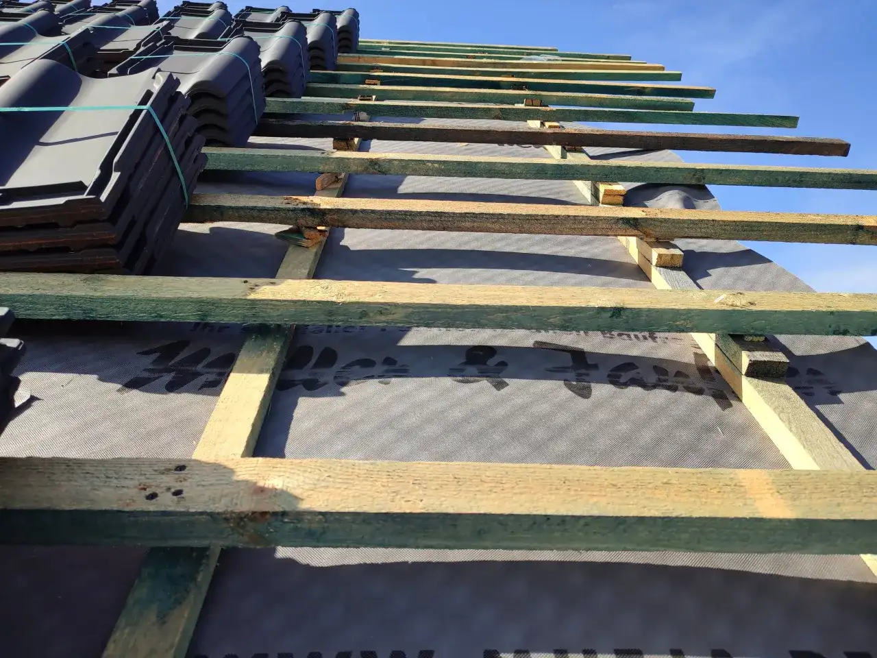 Uginajace sie panele podlogowe czekaja na montaz. Widoczna konstrukcja dachu z drewnianymi belkami i czarna membrana.