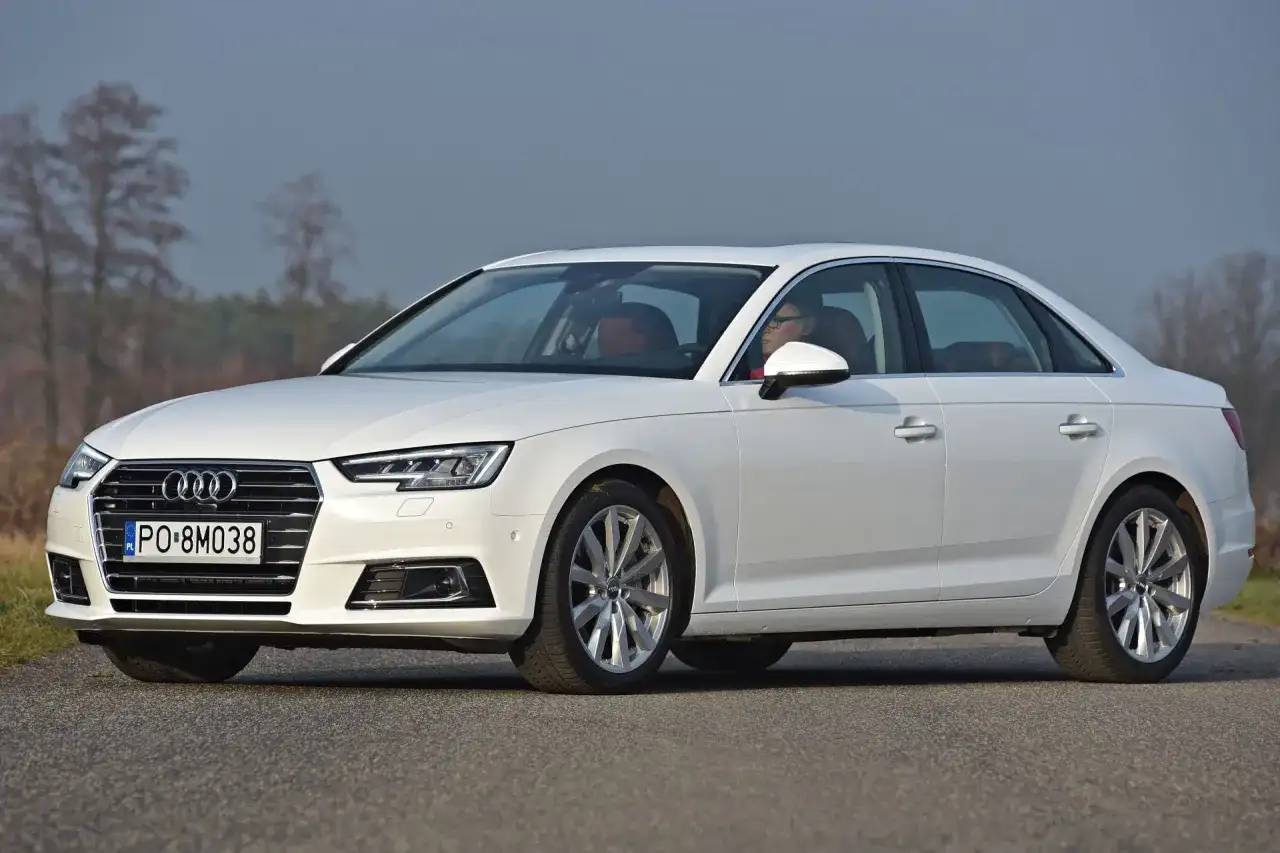 Białe Audi A4 sedan z kierowcą za kierownicą, zaparkowane na drodze.