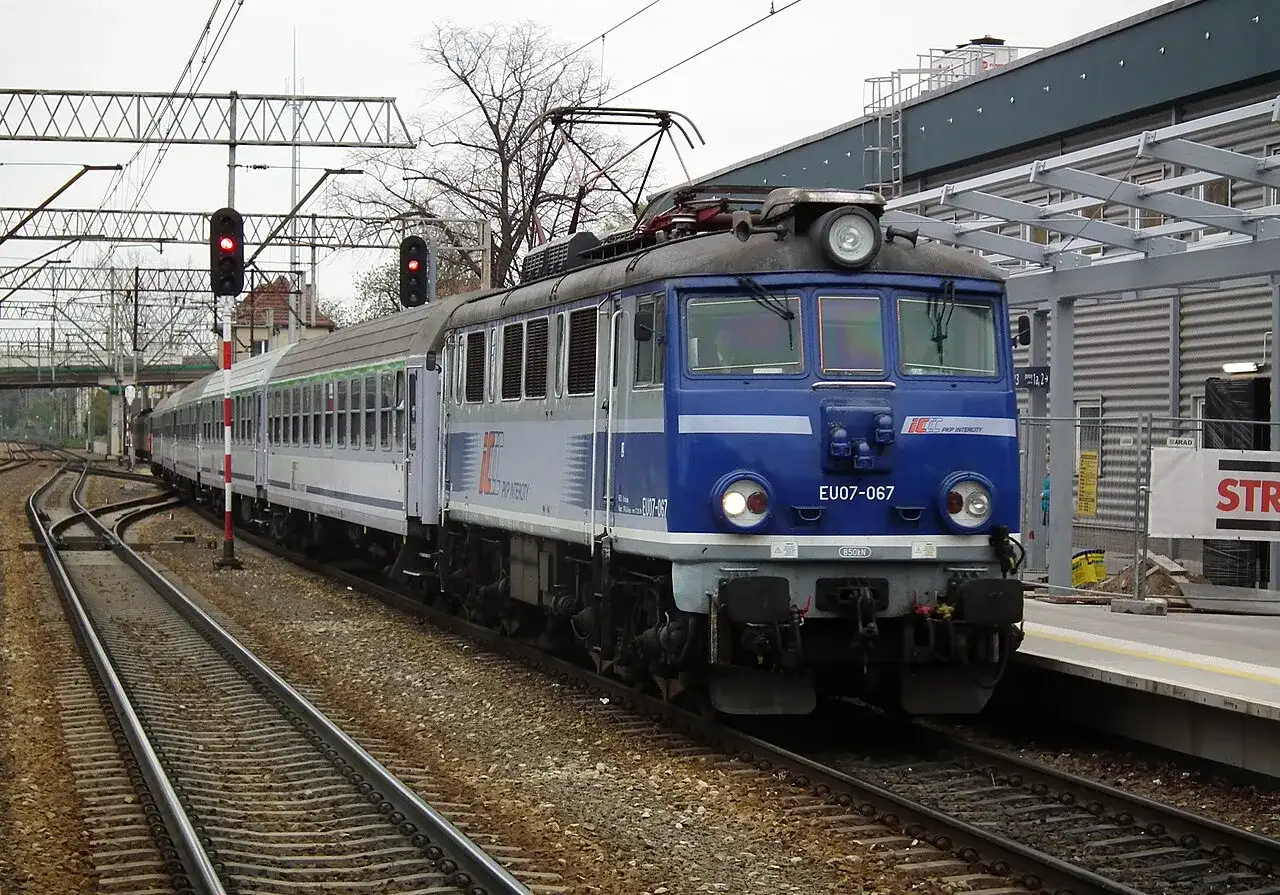 Niebieska lokomotywa EU07-067 PKP Intercity stoi na torach. Co oznacza TLK w pociągach? To oznaczenie tanich połączeń PKP Intercity.