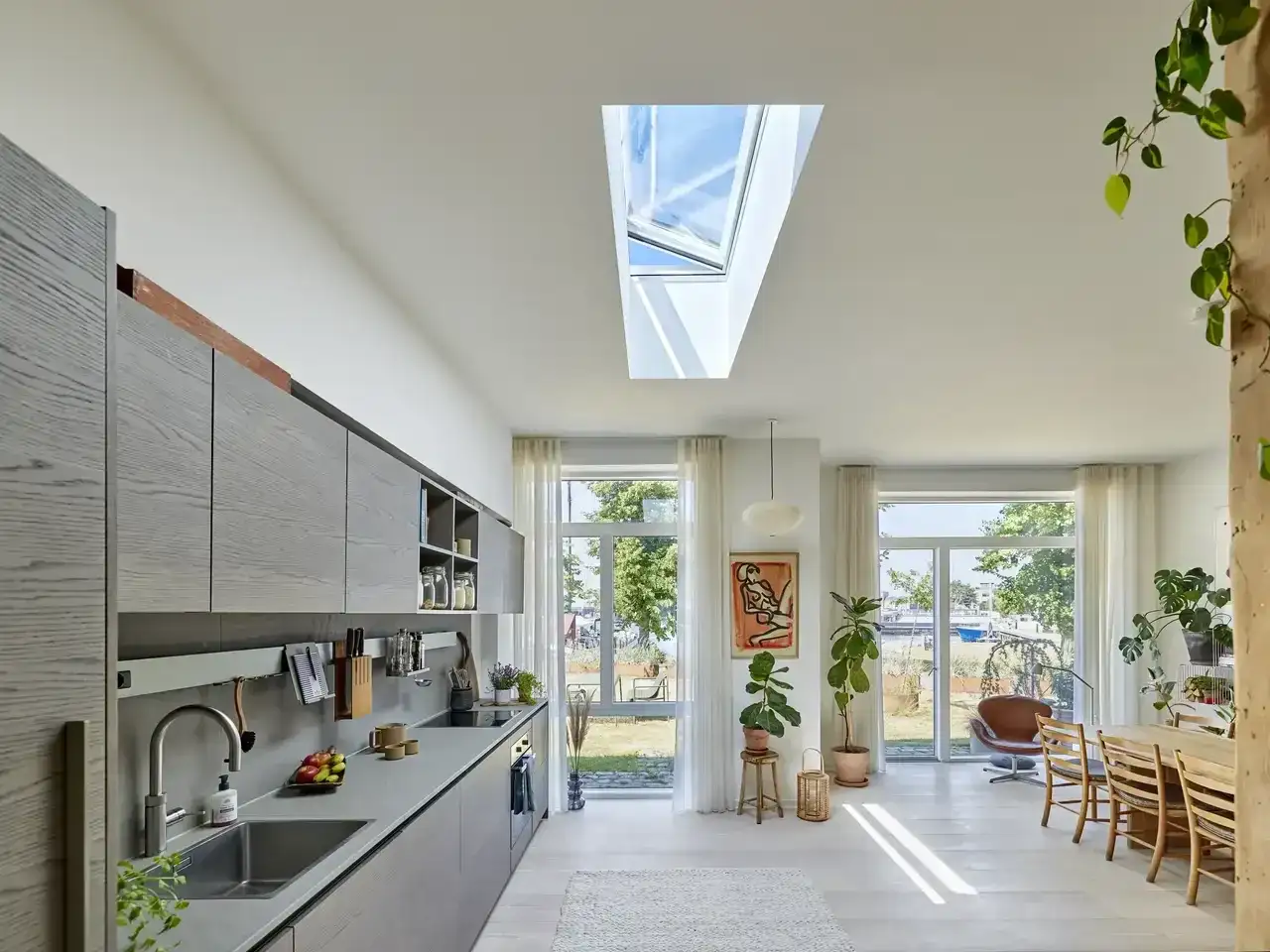 Nowoczesna kuchnia z wyspą i jadalnią, wszystko pod dachem. Światło wpada przez okna i świetlik.