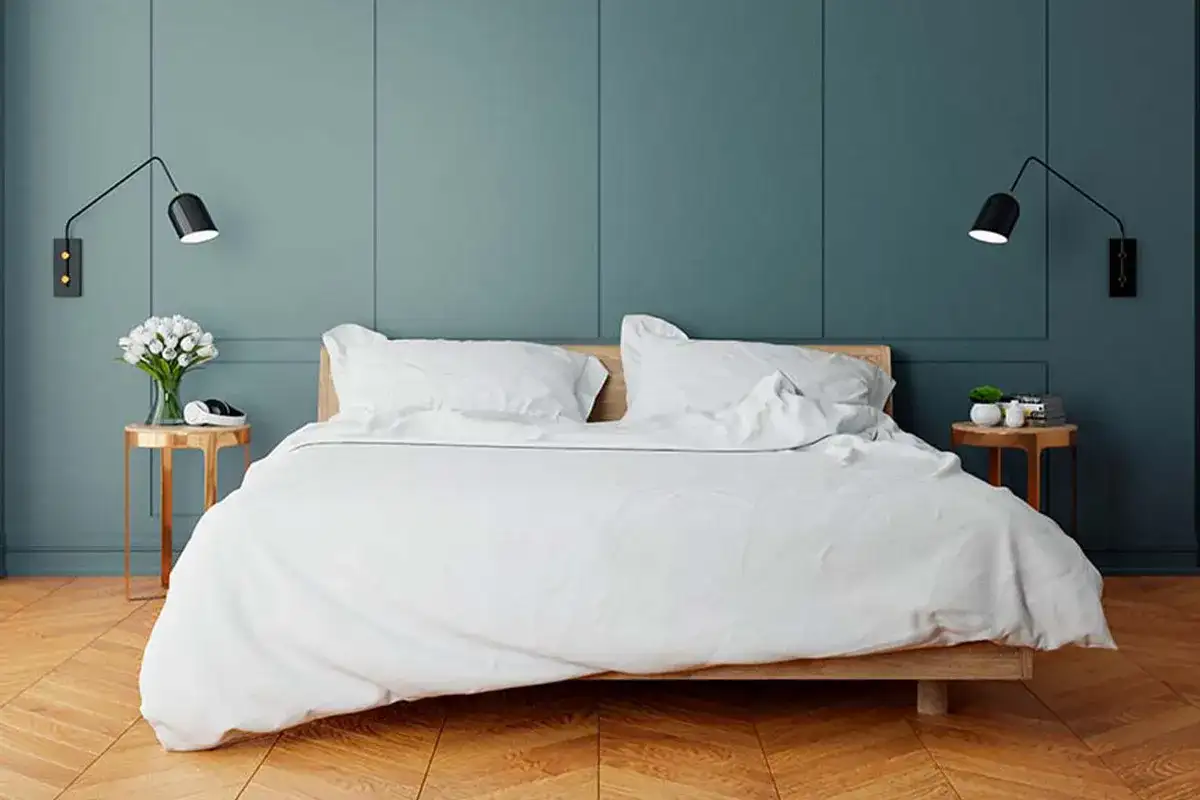 Elegancka sypialnia z białym pościelonym łóżkiem. Po obu stronach łóżka, na odpowiedniej wysokości, zamontowano czarne kinkiety, tworząc przytulną atmosferę.