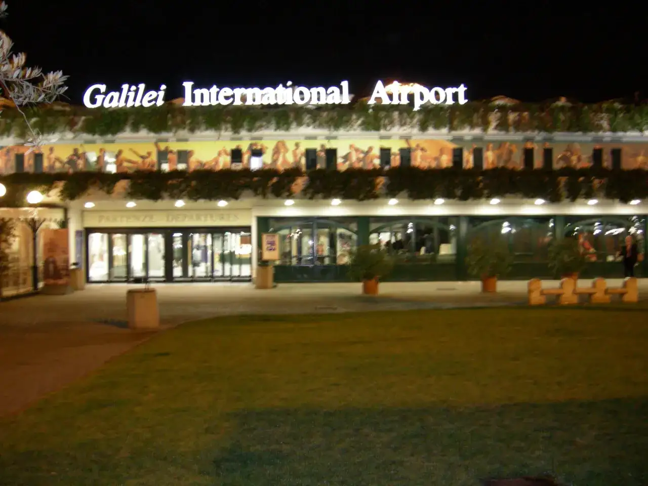 Port lotniczy Piza nocą. Jasny napis "Galilei International Airport" nad wejściem do terminalu.