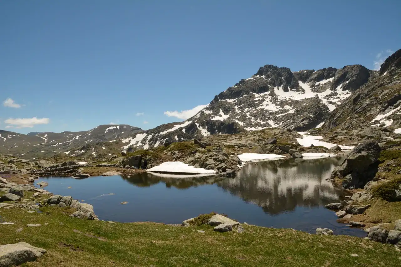 Góry Pirin z jeziorem odbijającym skaliste szczyty i resztki śniegu.