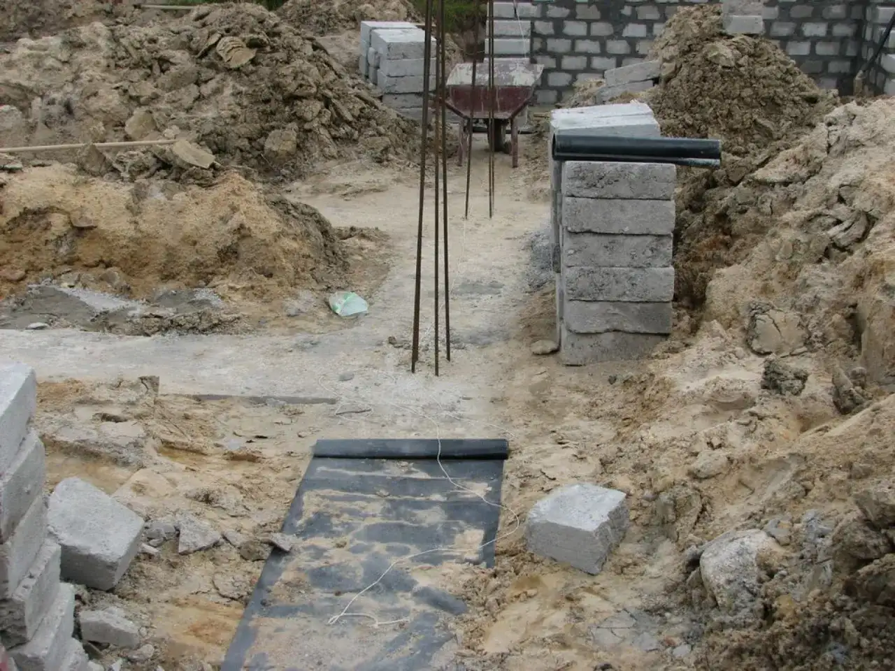 Budowa fundamentów: betonowe pustaki, zbrojenie, czarna folia izolacyjna i ziemia.