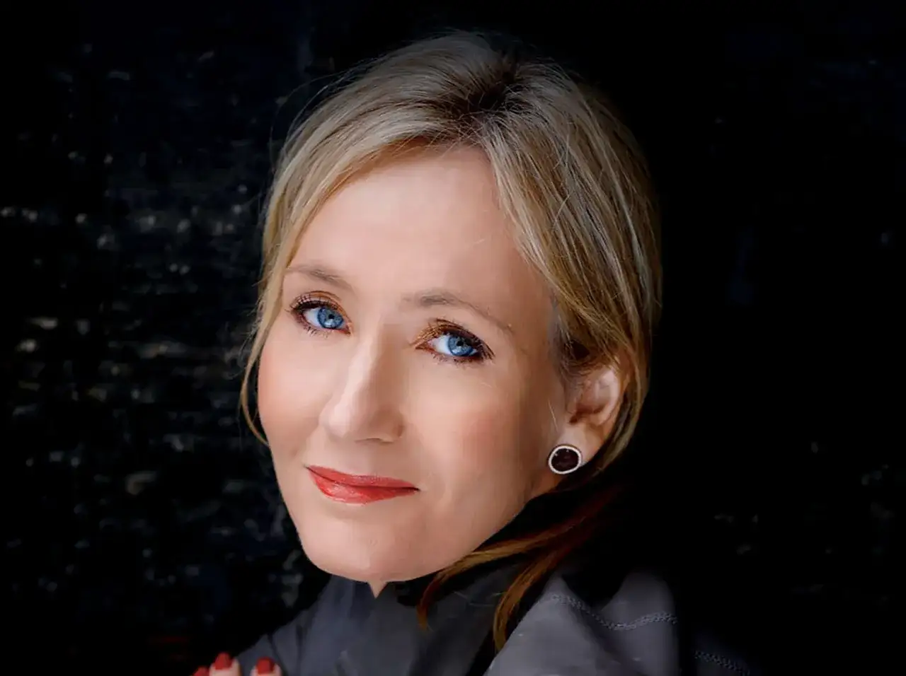 Portret J.K. Rowling, autorki książki Harry Potter, z jej charakterystycznymi niebieskimi oczami i uśmiechem.