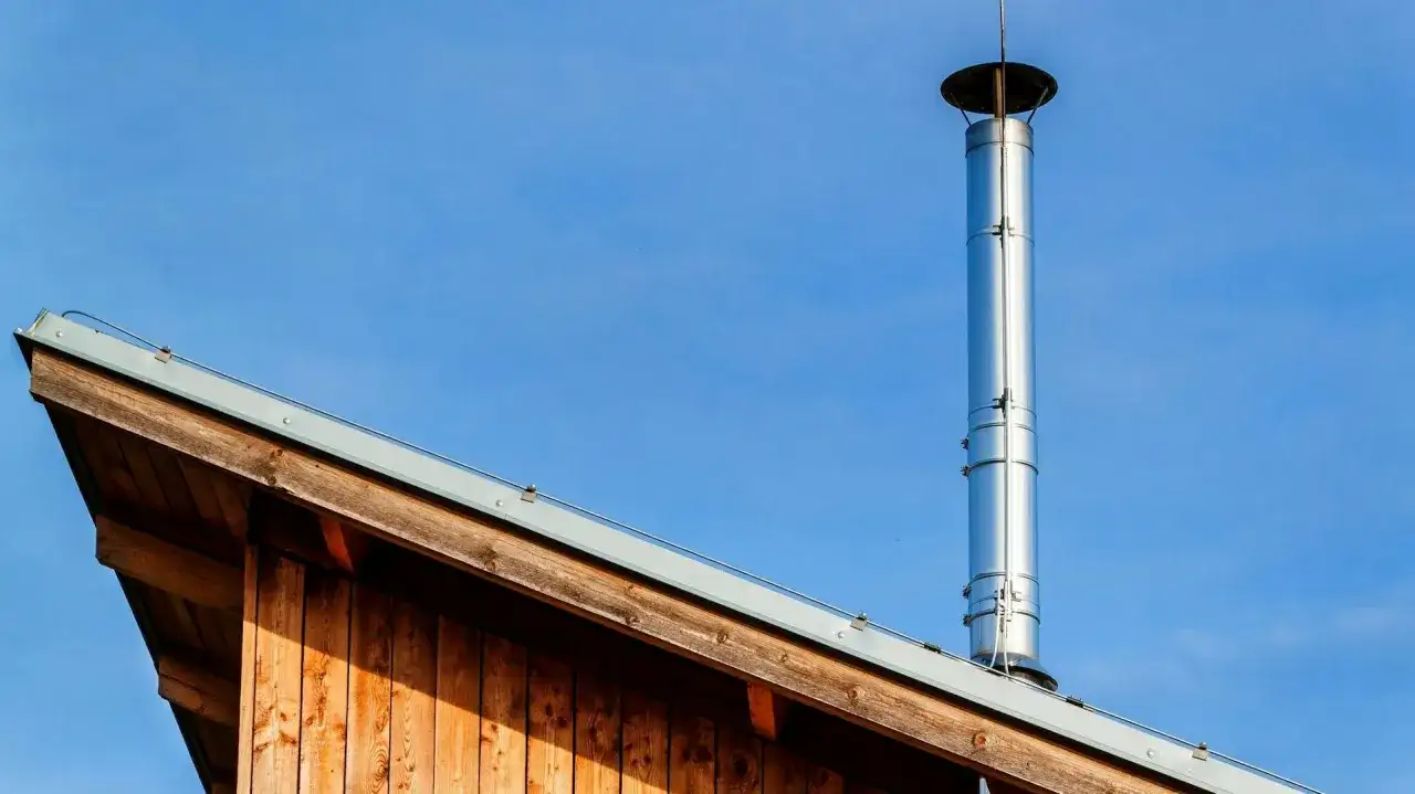 Błyszczące, zewnętrzne kominy do pieców co na tle błękitnego nieba, zamontowane na drewnianym dachu.