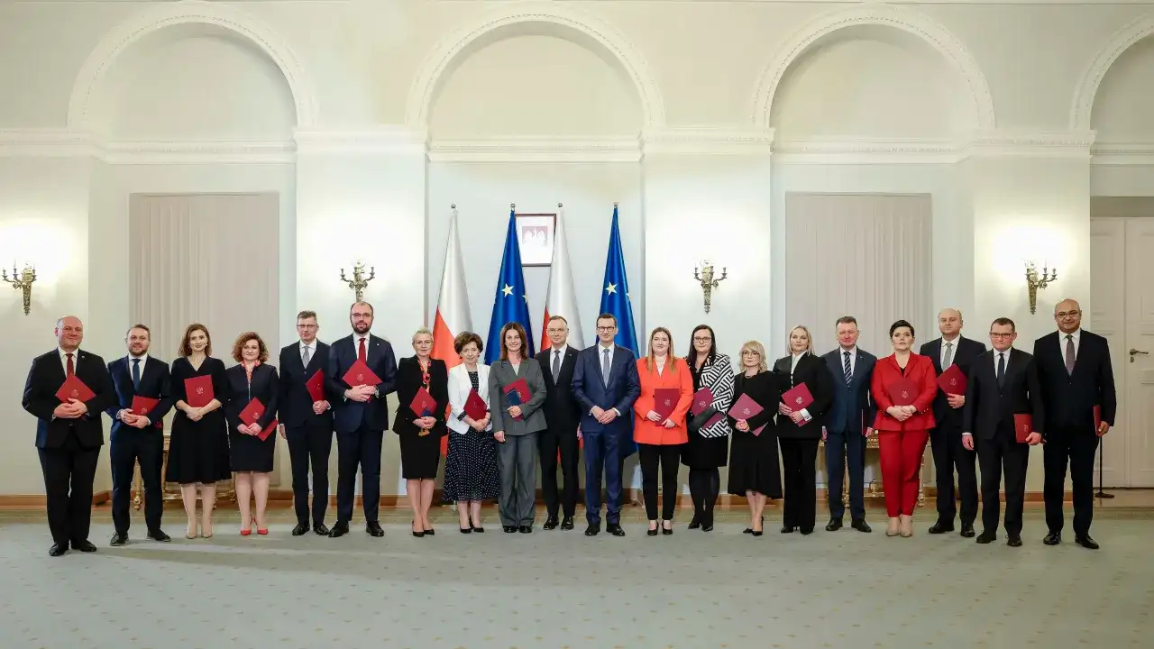 Grupa osób w eleganckich strojach, z flagami Polski w tle. Czy wśród nich jest premier Polski?