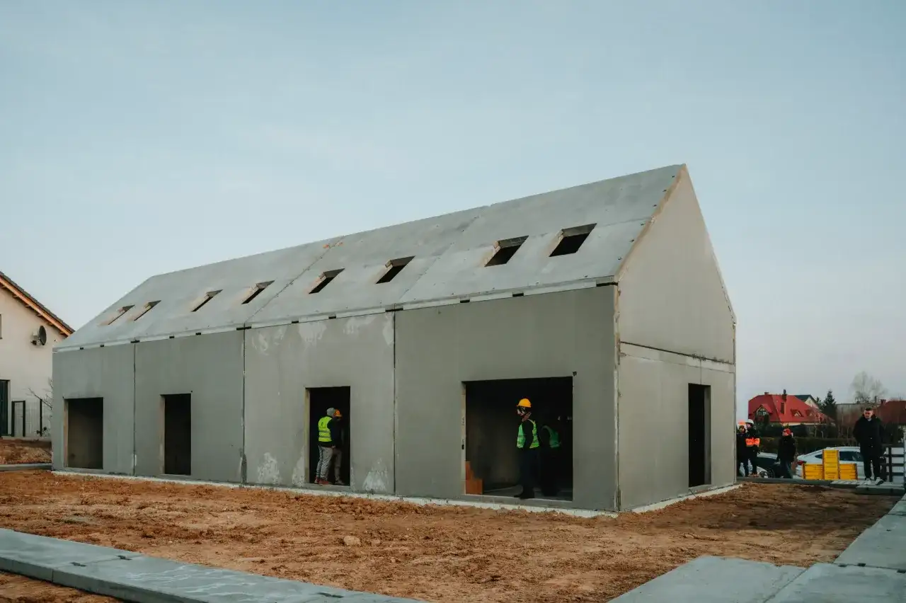 Budowa domu z gotowych elementów betonowych. Widać pracowników w kamizelkach odblaskowych.