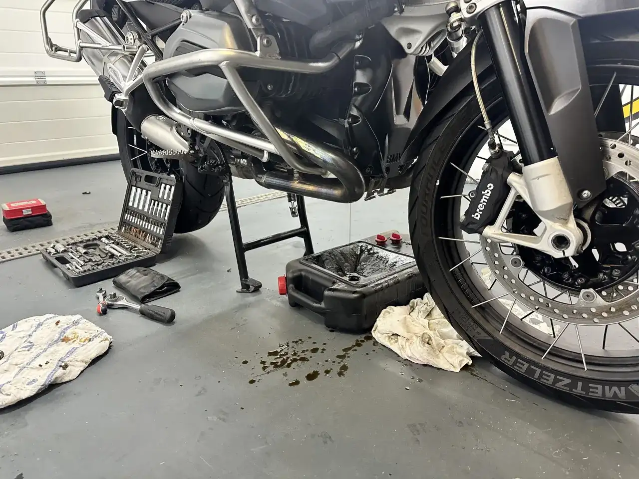 Motocykl na stojaku, narzędzia i pojemnik na zużyty olej.