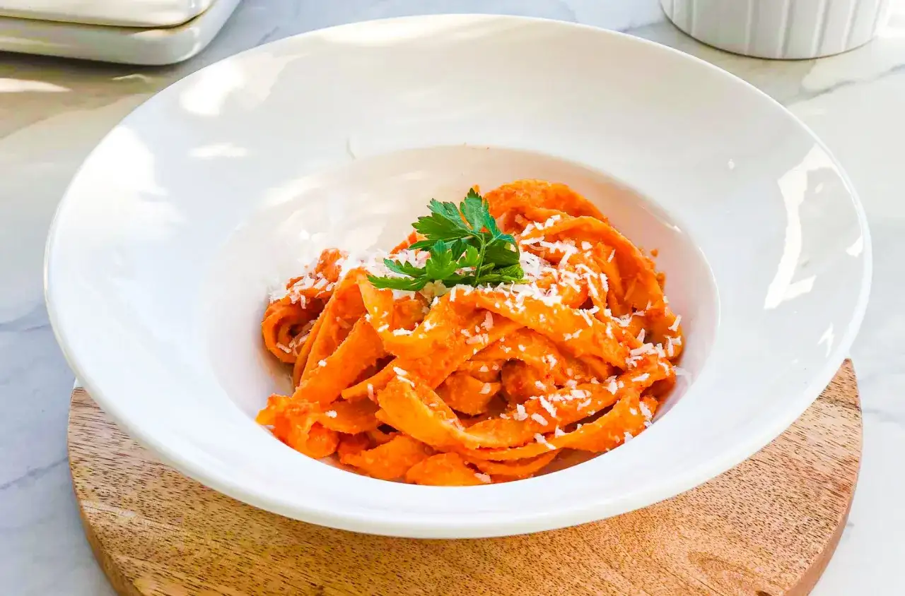 Pappardelle z kremowym sosem z pieczonej papryki, posypane parmezanem i udekorowane natką pietruszki. Pyszne danie, które zachwyca smakiem.