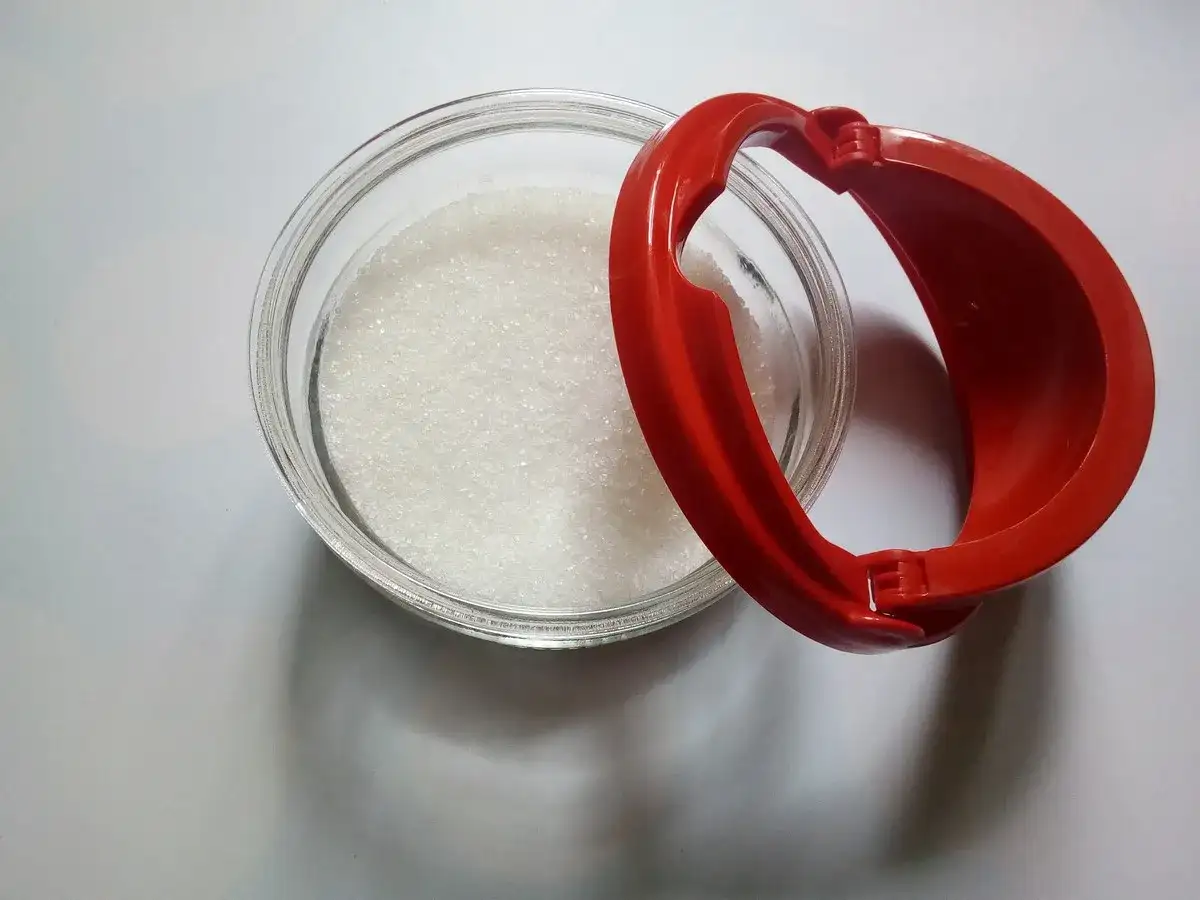 Szklana miska z cukrem i czerwona miarka w kształcie serca.