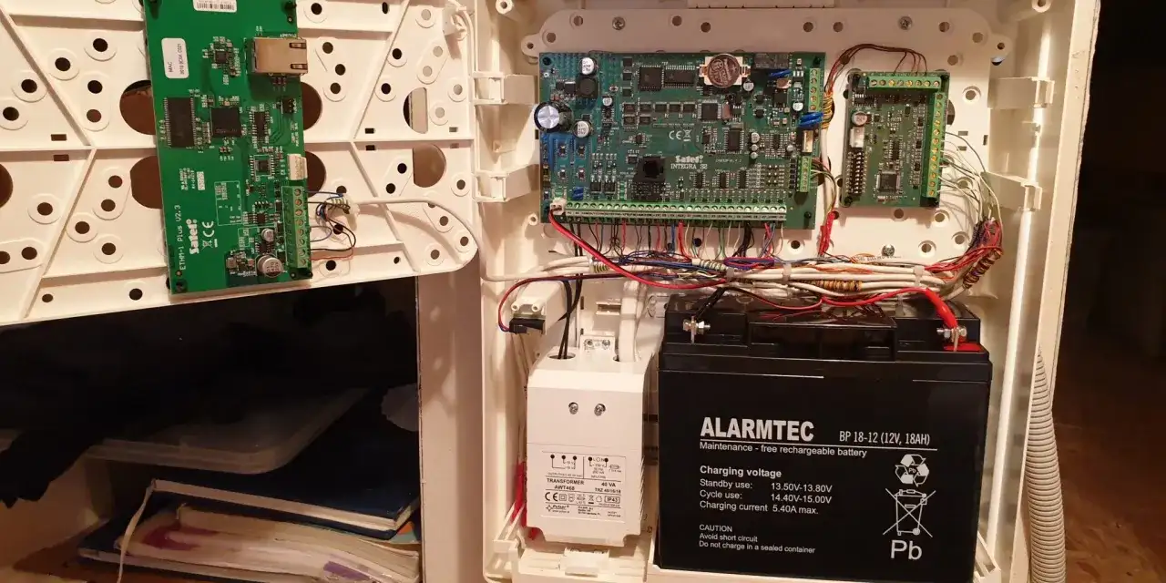 Wnętrze centrali alarmowej: płytki drukowane, transformator i akumulator. Schemat okablowania pokazuje, jak podłączyć alarm w domu.